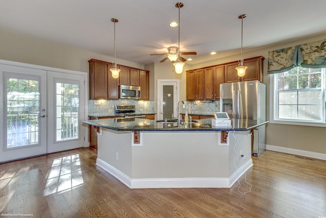 kitchen with french doors, sink, light wood-type flooring, an island with sink, and appliances with stainless steel finishes