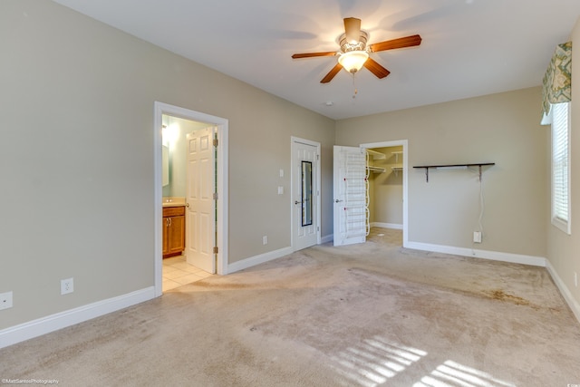 unfurnished bedroom with light carpet, a walk in closet, ensuite bathroom, ceiling fan, and a closet