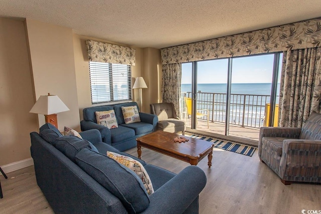 living room with plenty of natural light, a water view, a textured ceiling, and light hardwood / wood-style flooring