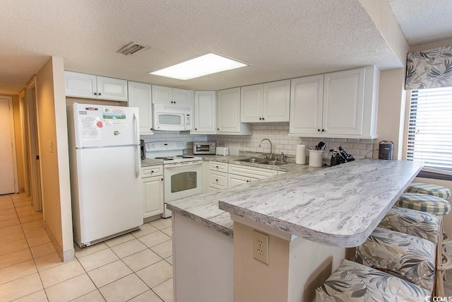 kitchen with kitchen peninsula, white appliances, sink, white cabinetry, and a breakfast bar area