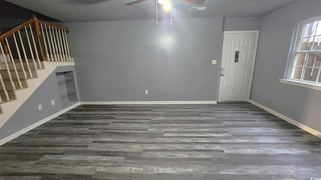 unfurnished living room with stairway, baseboards, visible vents, and dark wood finished floors