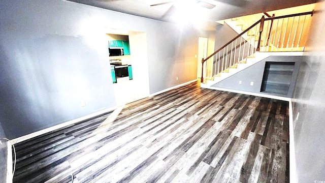 unfurnished living room featuring dark wood-style floors, a ceiling fan, baseboards, and stairs