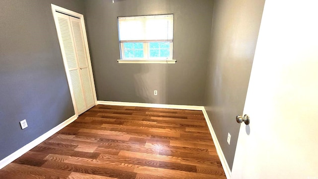 unfurnished bedroom with a closet, baseboards, and dark wood-type flooring