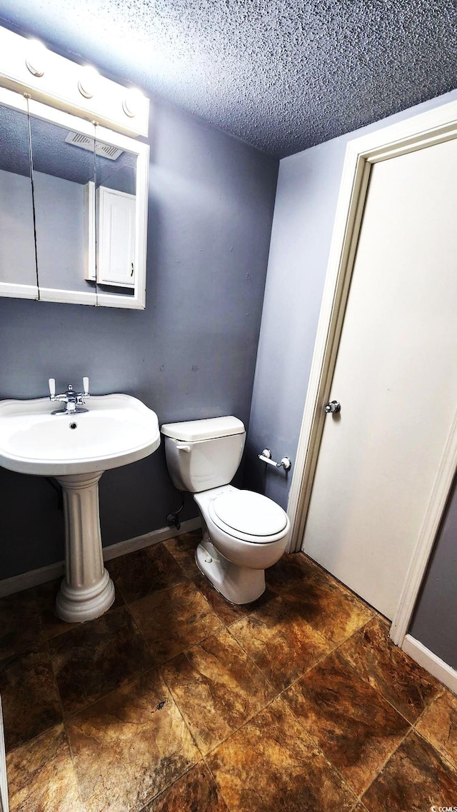 half bathroom featuring visible vents, baseboards, a textured ceiling, and toilet