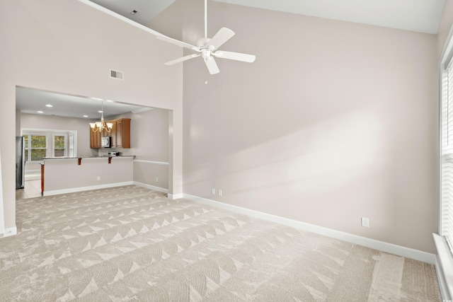 unfurnished living room featuring high vaulted ceiling, light colored carpet, and ceiling fan with notable chandelier