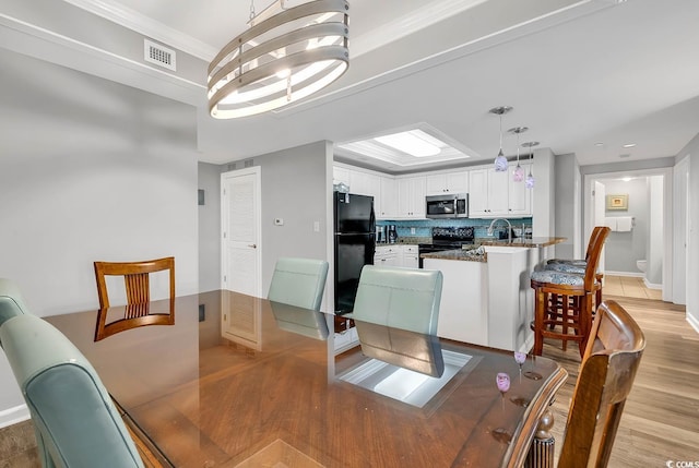 dining area with light wood-type flooring, ornamental molding, and an inviting chandelier