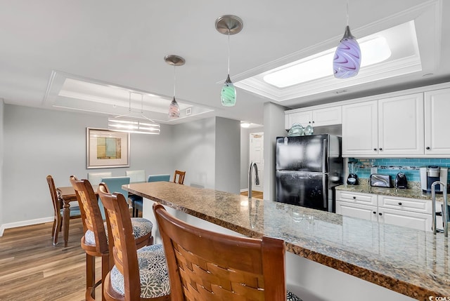 kitchen with white cabinets, backsplash, a tray ceiling, and black fridge