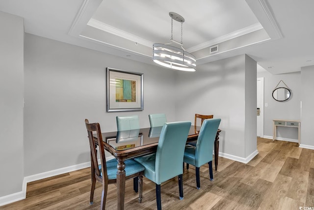 dining area with hardwood / wood-style floors, a raised ceiling, ornamental molding, and an inviting chandelier