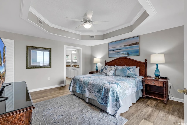 bedroom featuring a raised ceiling, ceiling fan, ensuite bathroom, and wood-type flooring