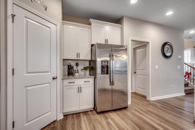 kitchen featuring light stone counters, white cabinets, light hardwood / wood-style floors, and stainless steel refrigerator with ice dispenser