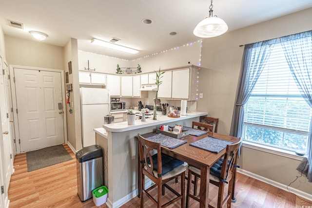 kitchen with kitchen peninsula, pendant lighting, light hardwood / wood-style flooring, white fridge, and white cabinetry