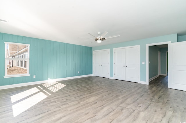 unfurnished bedroom with ceiling fan, light wood-type flooring, and two closets