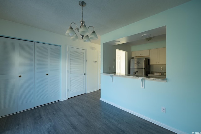 kitchen featuring dark hardwood / wood-style flooring, decorative light fixtures, white cabinetry, stainless steel refrigerator, and a breakfast bar area