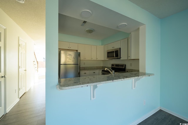 kitchen with a kitchen breakfast bar, light wood-type flooring, a textured ceiling, appliances with stainless steel finishes, and kitchen peninsula