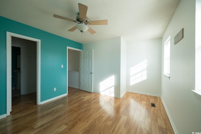 unfurnished bedroom featuring a spacious closet, ceiling fan, wood-type flooring, a textured ceiling, and a closet