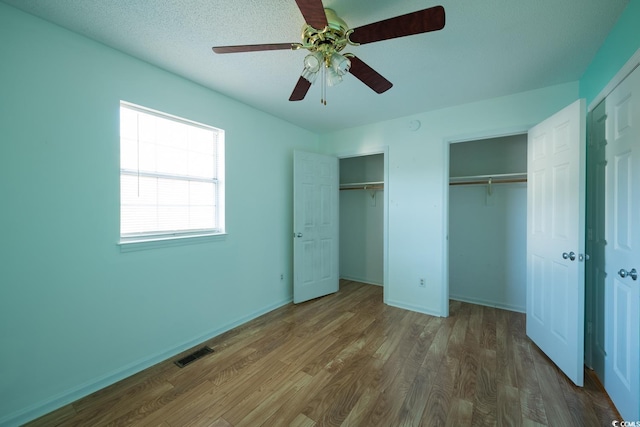 unfurnished bedroom featuring a textured ceiling, ceiling fan, wood-type flooring, and two closets