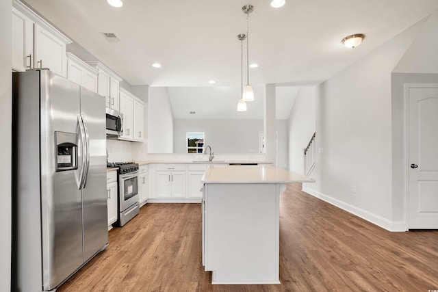 kitchen with kitchen peninsula, appliances with stainless steel finishes, pendant lighting, white cabinets, and light wood-type flooring