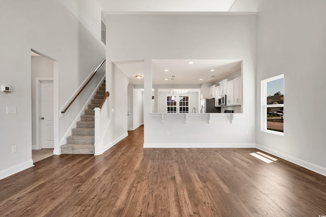 unfurnished living room featuring dark hardwood / wood-style flooring, a high ceiling, and an inviting chandelier