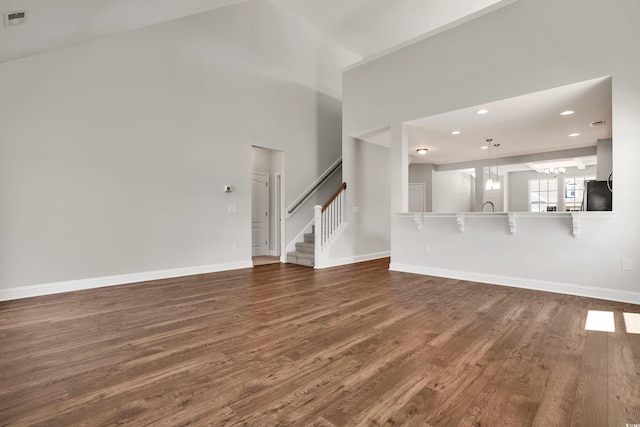 unfurnished living room featuring a towering ceiling, dark hardwood / wood-style flooring, and an inviting chandelier