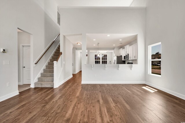 unfurnished living room with a towering ceiling, an inviting chandelier, and dark wood-type flooring