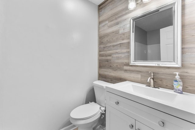 bathroom featuring vanity, toilet, and wooden walls