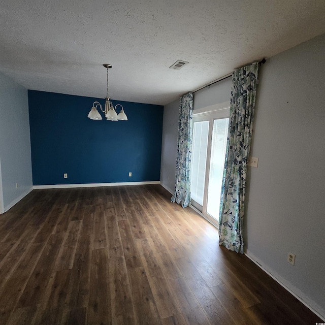 spare room featuring a textured ceiling, a notable chandelier, and dark wood-type flooring