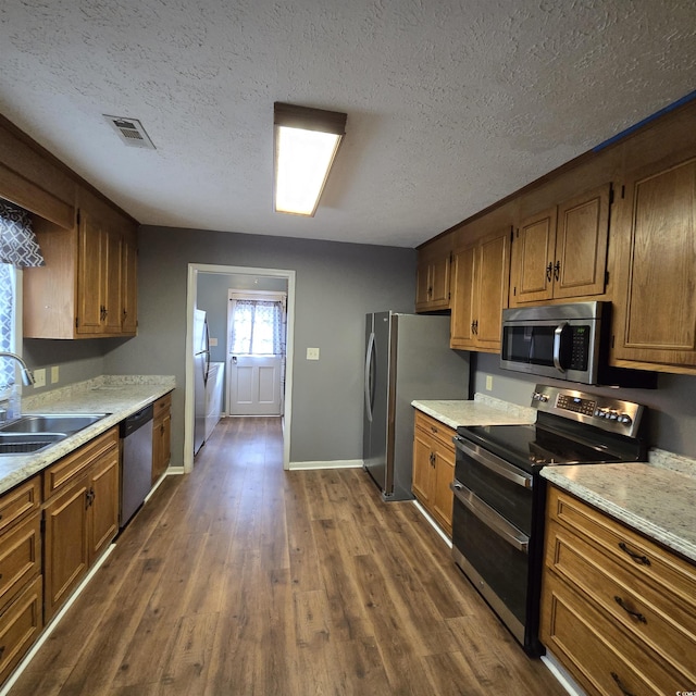 kitchen with appliances with stainless steel finishes, a textured ceiling, dark wood-type flooring, and sink