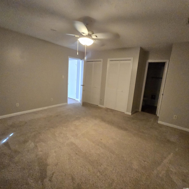 unfurnished bedroom featuring a textured ceiling, ceiling fan, carpet, and two closets