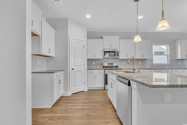 kitchen with light stone counters, a sink, stainless steel appliances, white cabinetry, and light wood-type flooring