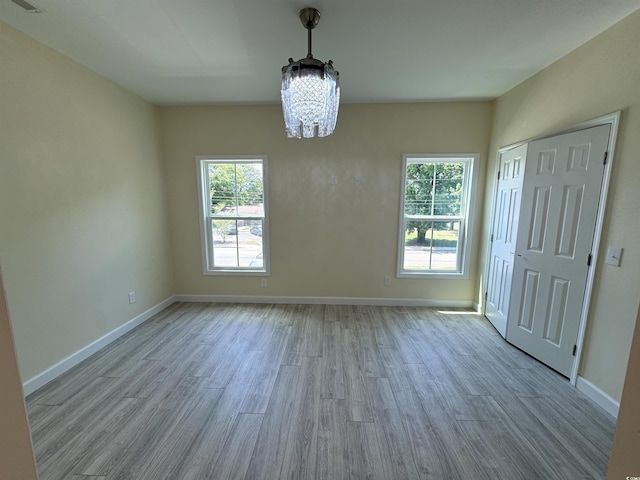 unfurnished dining area with a chandelier, a wealth of natural light, and light hardwood / wood-style flooring