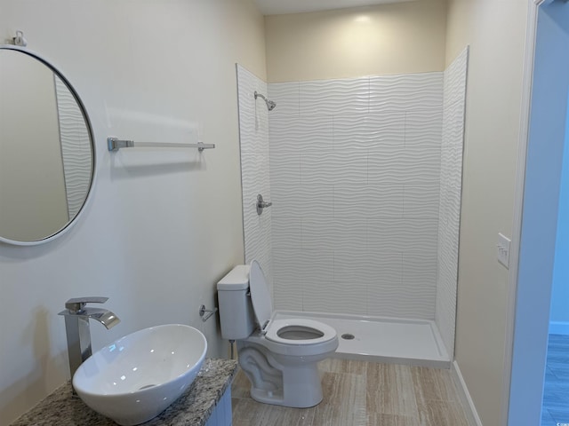 bathroom featuring a tile shower, sink, wood-type flooring, and toilet