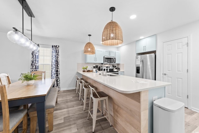 kitchen featuring white cabinetry, kitchen peninsula, light hardwood / wood-style floors, decorative light fixtures, and appliances with stainless steel finishes