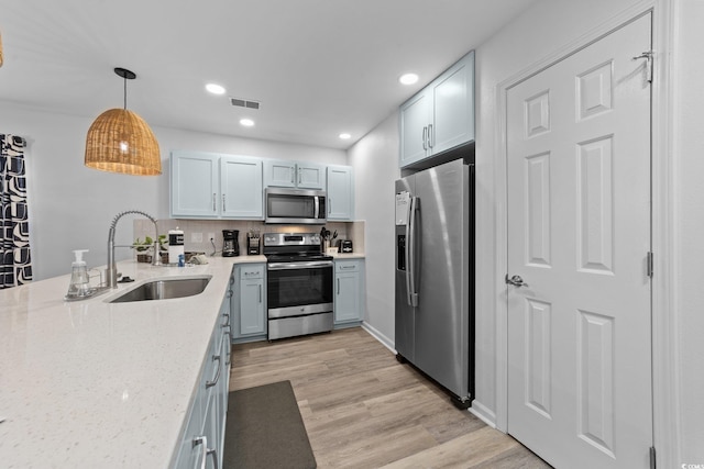 kitchen featuring appliances with stainless steel finishes, sink, white cabinets, light hardwood / wood-style floors, and hanging light fixtures