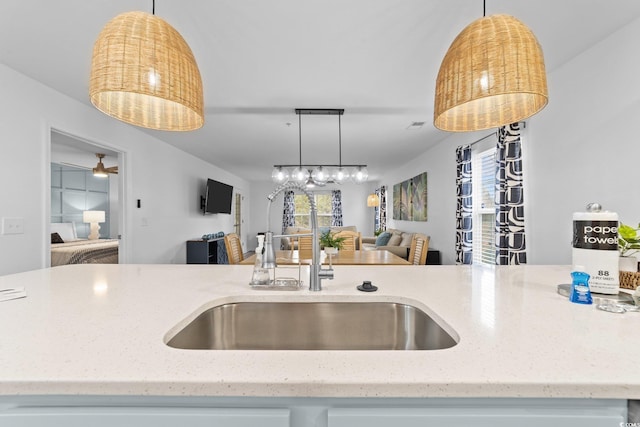 kitchen featuring light stone counters, sink, ceiling fan, and decorative light fixtures