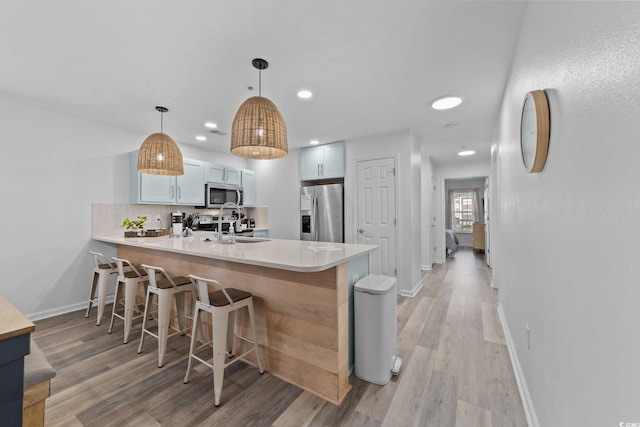 kitchen featuring kitchen peninsula, stainless steel appliances, white cabinetry, and hanging light fixtures