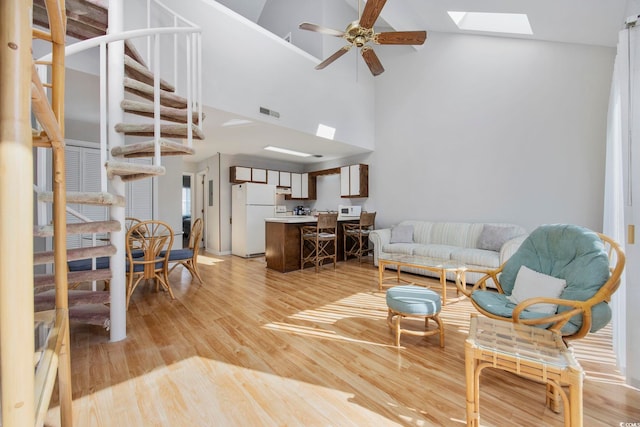 living room featuring ceiling fan, light wood-type flooring, high vaulted ceiling, and a skylight