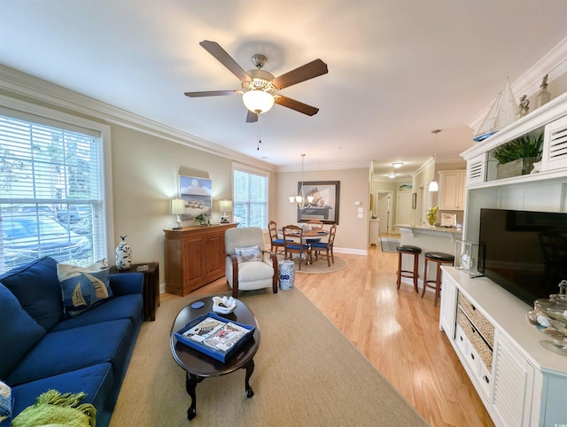 living room featuring ceiling fan with notable chandelier, ornamental molding, light wood-type flooring, and a healthy amount of sunlight