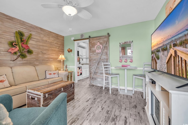 interior space featuring ceiling fan, sink, a barn door, light hardwood / wood-style floors, and wooden walls