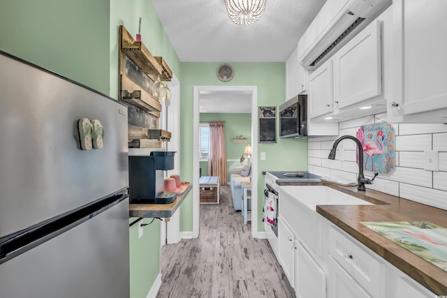 kitchen with stainless steel appliances, butcher block countertops, light hardwood / wood-style floors, a textured ceiling, and white cabinets