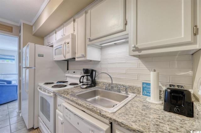 kitchen featuring white appliances, crown molding, sink, light tile patterned floors, and white cabinetry