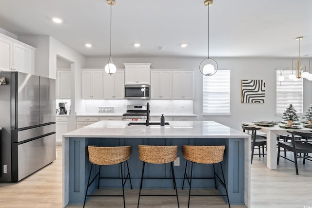 kitchen with hanging light fixtures, stainless steel appliances, and a center island with sink