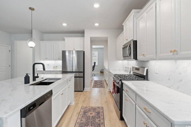 kitchen with light wood-type flooring, stainless steel appliances, sink, white cabinets, and hanging light fixtures