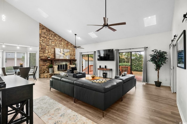 living room featuring ceiling fan, a skylight, high vaulted ceiling, and light hardwood / wood-style flooring