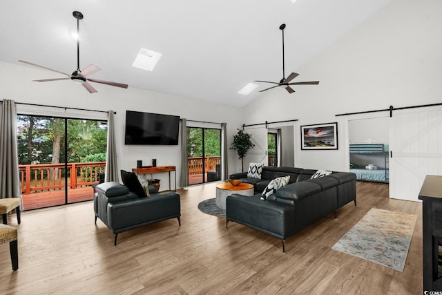 living room featuring a barn door, a skylight, high vaulted ceiling, and light hardwood / wood-style floors