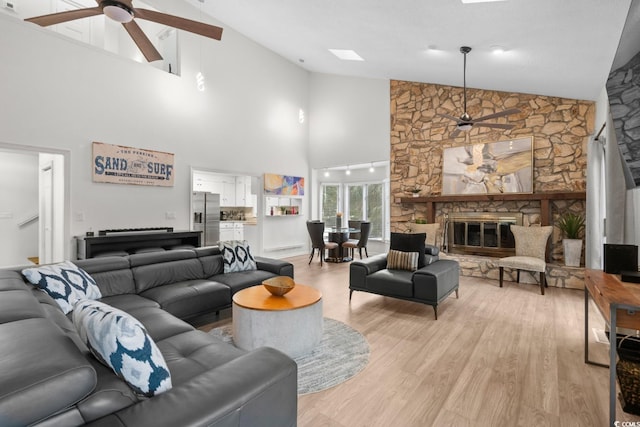 living room with ceiling fan, light hardwood / wood-style floors, a fireplace, and high vaulted ceiling