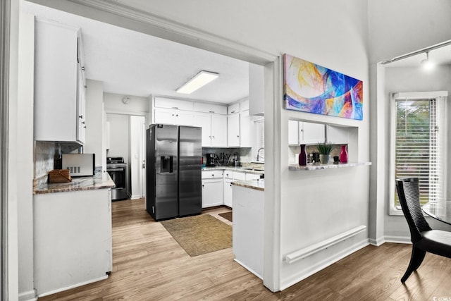 kitchen with white cabinetry, stainless steel electric range oven, tasteful backsplash, black fridge, and light hardwood / wood-style flooring