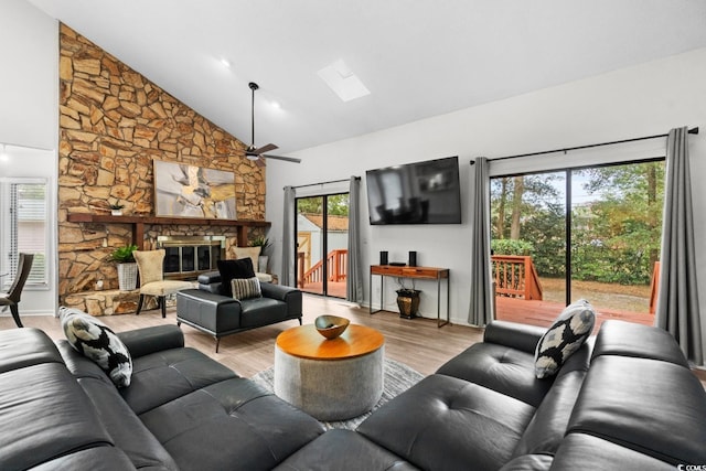 living room with a skylight, plenty of natural light, a stone fireplace, and light wood-type flooring