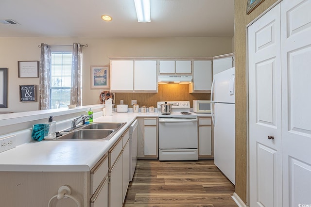 kitchen with under cabinet range hood, a sink, white appliances, a peninsula, and dark wood-style flooring