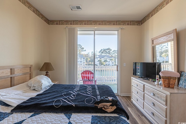 bedroom with wood finished floors, visible vents, baseboards, and access to exterior