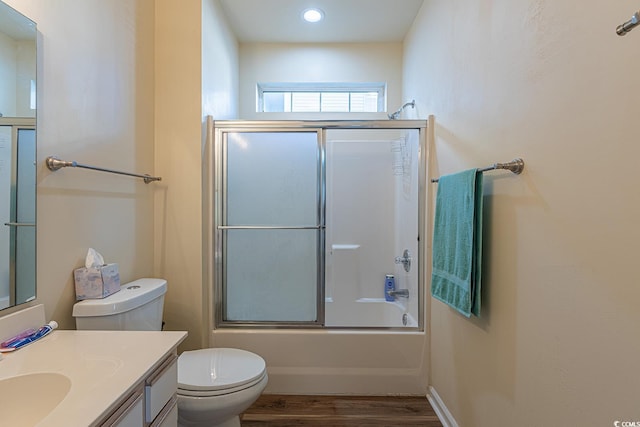 bathroom with recessed lighting, wood finished floors, combined bath / shower with glass door, toilet, and vanity
